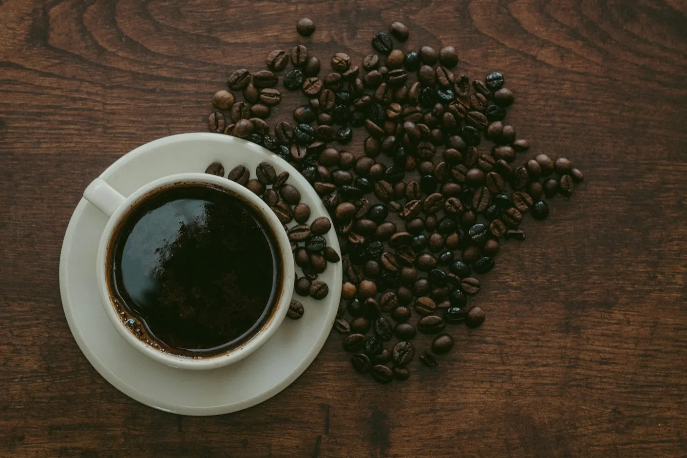 Cup of black coffee surrounded by whole coffee beans on a wooden bench
