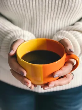 Hands holding an orange ceramic mug of coffee