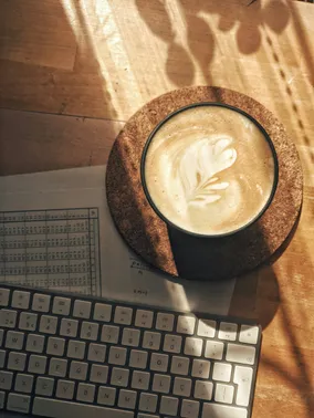 Latte art in a cup on a cork coaster beside a laptop