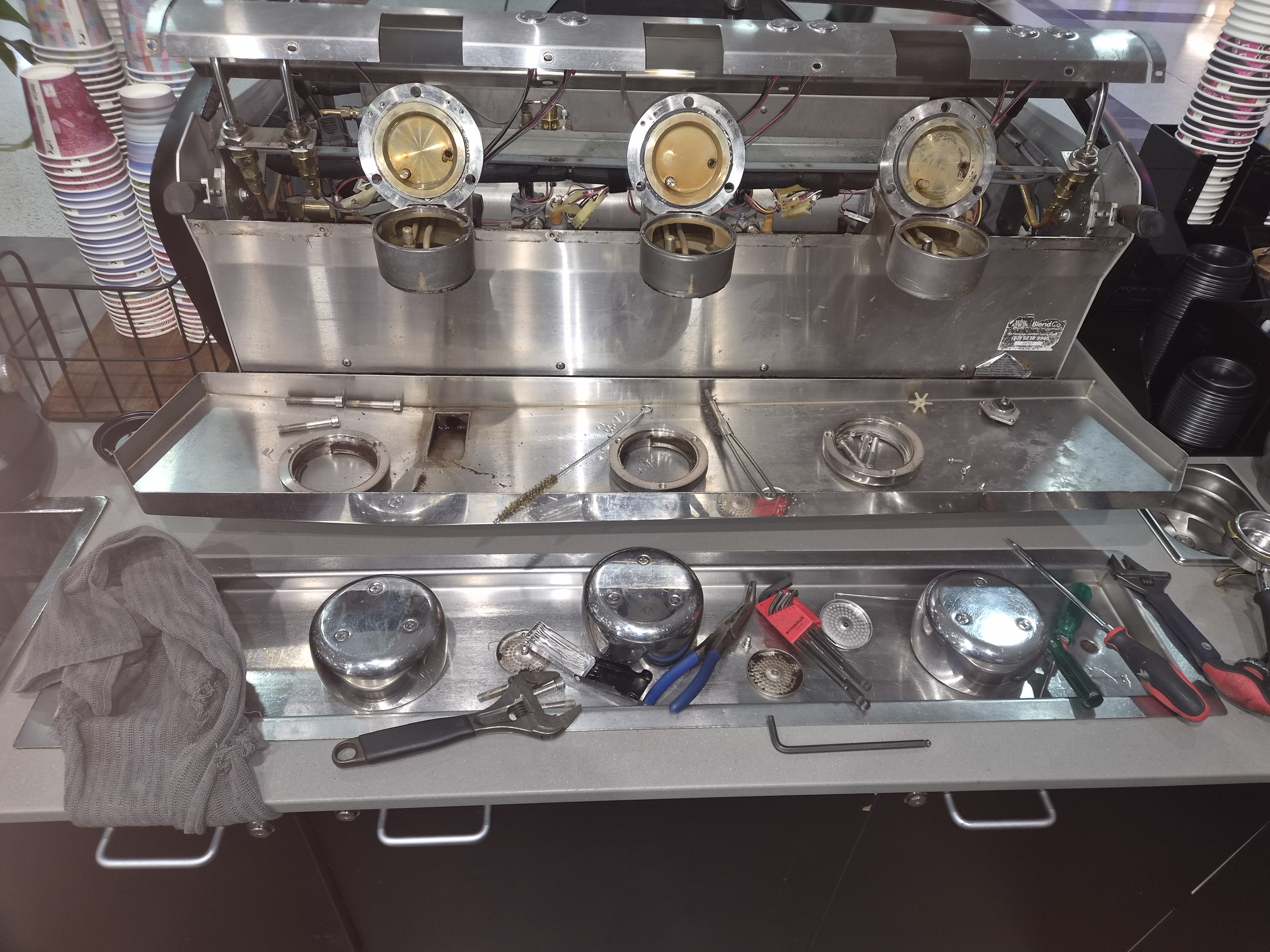 Three-group commercial espresso machine stripped down on Paul's workshop bench, group seals and dispersion screens laid out beside the service tools